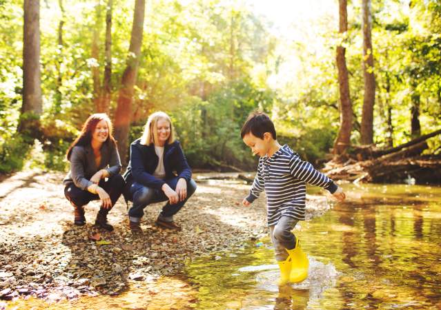 A lesbian couple watching their son play in a creek