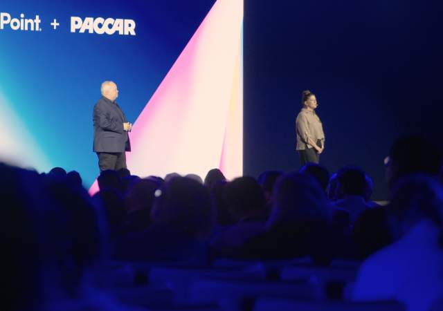 Two executives speaking in front of a room of hundreds of attendees.