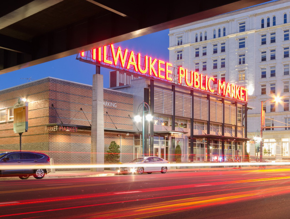 An exterior shot of the Milwaukee Public Market at dusk with the lights of the sign showing bright red against the sky
