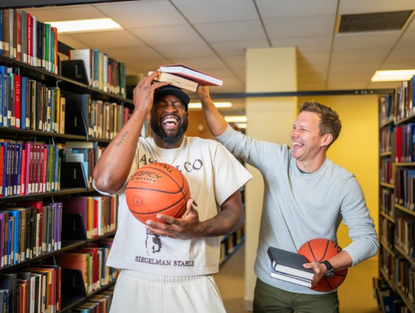 Wade & Diener in a library laughing, holding basketballs and books. Deiener holding books on Wade's head.