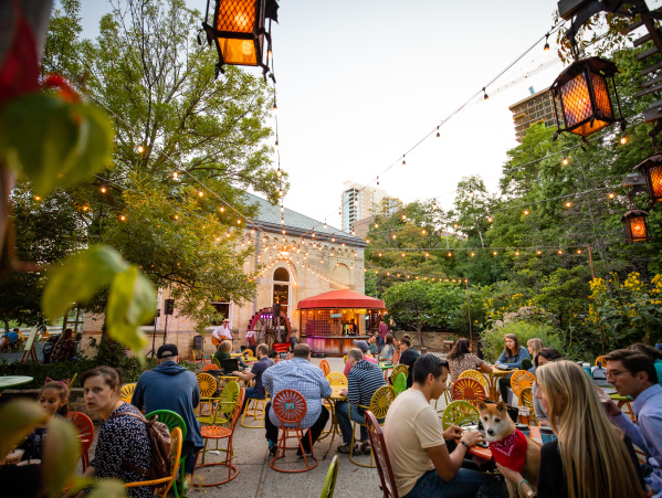Lively outdoor patio at Colectivo Coffee on the Lake with colorful chairs, string lights, trees, and people dining under evening light.