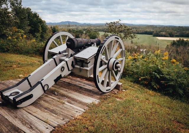 a replica Revolutionary war cannon points out at a sprawling field
