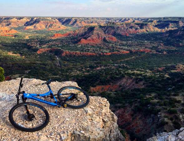 mountain bike laying on top of a cliff overlooking palo duro canyon