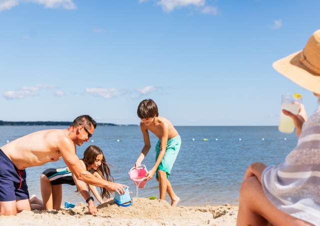 Family playing in sand while mom watches on Yorktown Beach