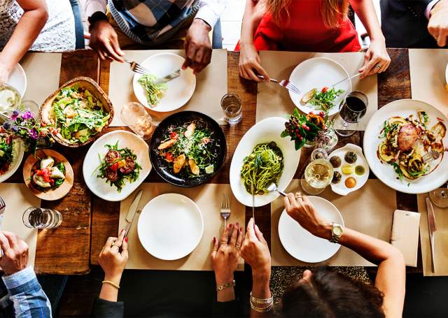 People eating from many plates of food on a table in a restaurant