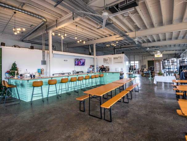 A row of stools line up to a teal bar. There are additional tables and benches throughout the room.