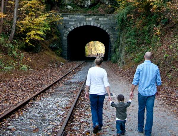 A small child holds hands with their parents as they walk along the rail trail toward Howard Tunnel in fall