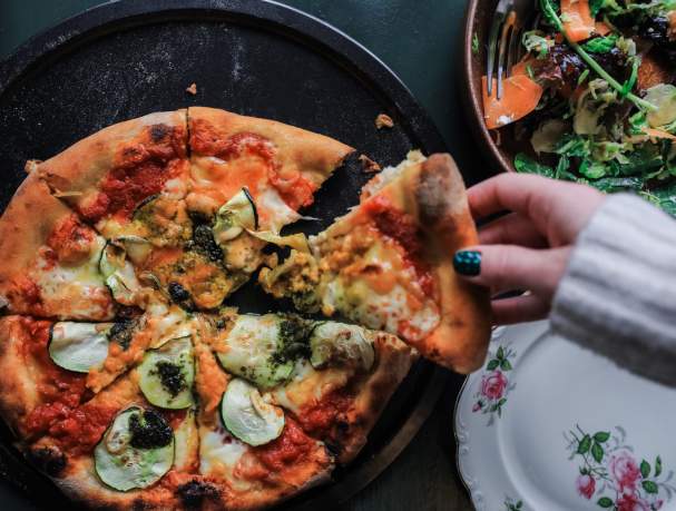 Female hand grabbing slice of pizza from tray