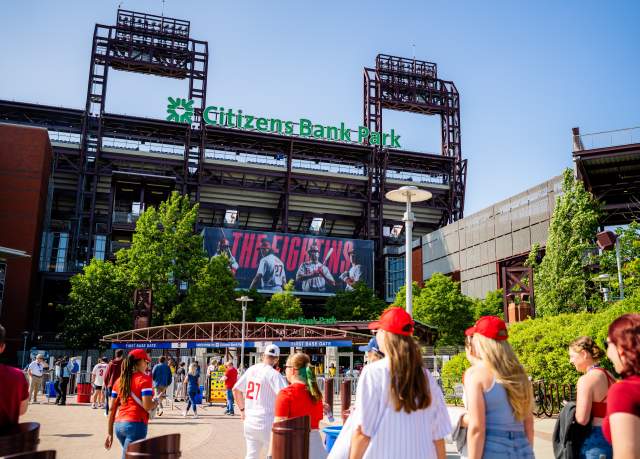 People wearing red hats and summer attire walking into the front entrance of Citizens Bank Park in Philadelphia