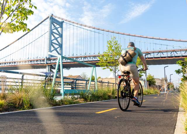 A person riding a bike on a trail with a large bridge in the background