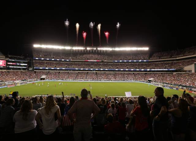 Fireworks blasting over a stadium at night filled with people