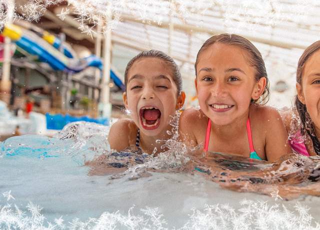 Three young girls in a pool in an indoor waterpark smiling