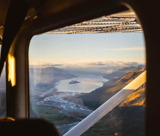 View from a plane window at sunrise looking out rivers, lakes and mountain ranges