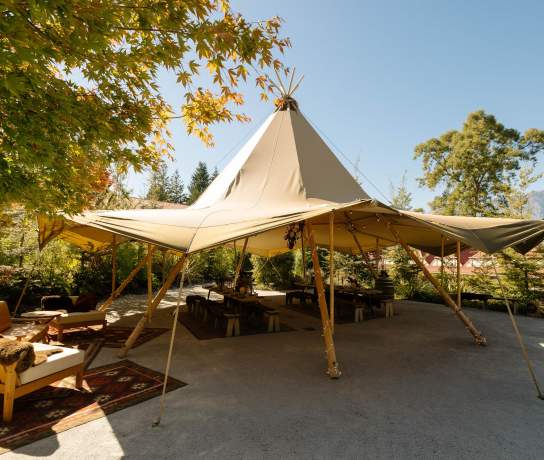 An image of a tipi setup for a dinner event outside with trees and sunny sky