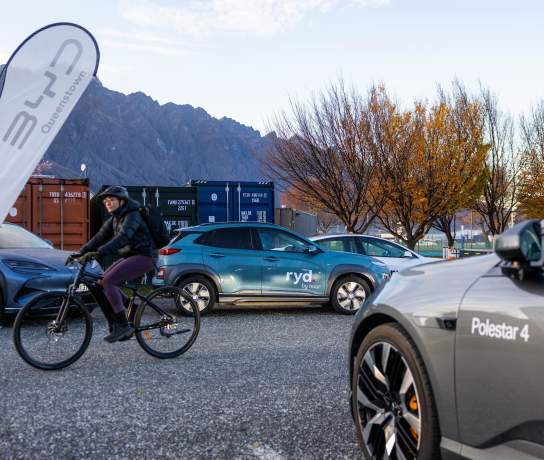 Electric cars out for display with the Remarkable Mountain range in the background and a person on an electric bike riding through the frame