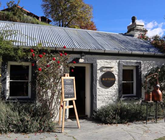 The outside of a white brick cottage with signs out the front for gin tasting