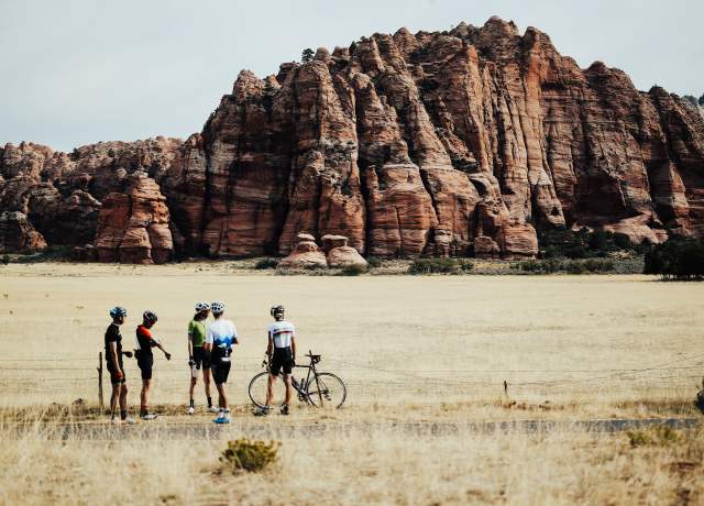 Five cyclists stand in front of a red rock formation in Kanarraville, Utah.