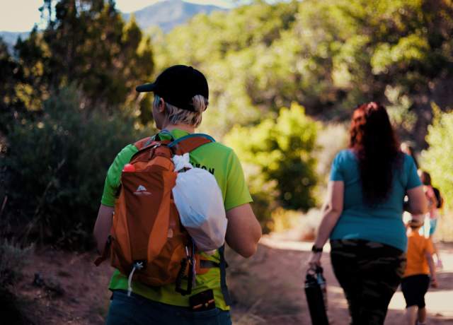 Family hiking through a red rock canyon on the Spring Creek Trail in Kanarraville Utah. A woman in the foreground has a small white trash bag attached to her bag for picking up litter.