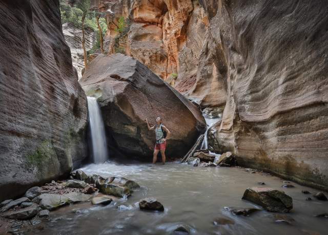 Woman standing beside a waterfall within a red rock slot canyon in southern Utah.