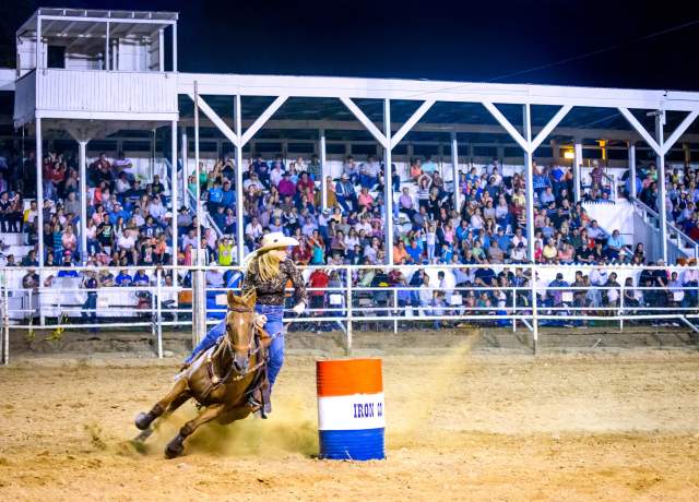 A barrel racer rounds a red, white, and blue barrel in front of a full stadium at the Iron County Fair in Parowan, Utah.