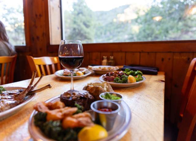 A table laid out with steaks, steamed vegetables, and a glass of red wine at Milts Stage Stop in Cedar City.