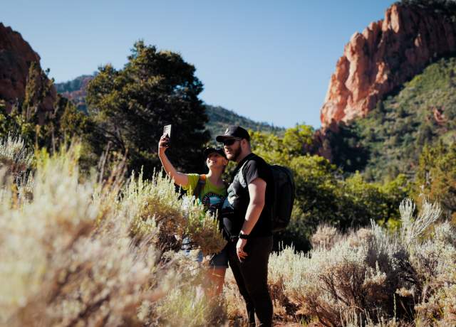 Couple taking a selfie on the Spring Creek Trail in Kanarraville, Utah with red rock formations in the background, surrounded by pale sagebrush.