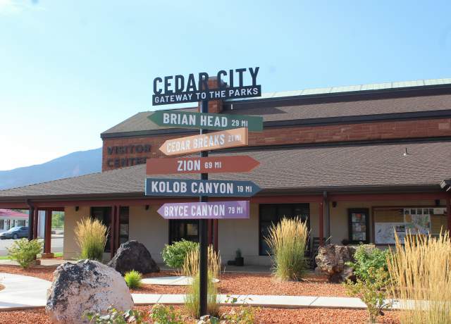 A brightly colored wayfinding sign pointing to nearby national parks and monuments standing in front of the Cedar City Visitor Center.