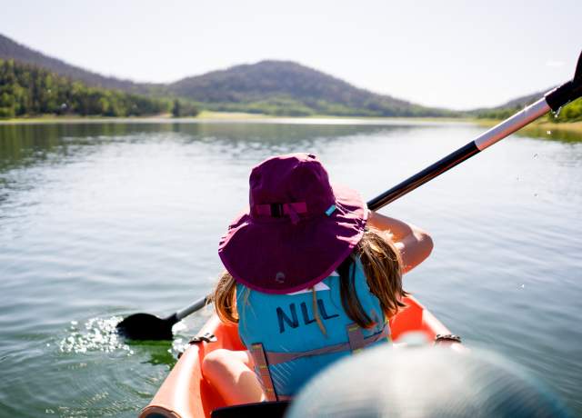 Person in a purple hat and bright blue life preserver kayaks on Navajo Lake in Southern Utah