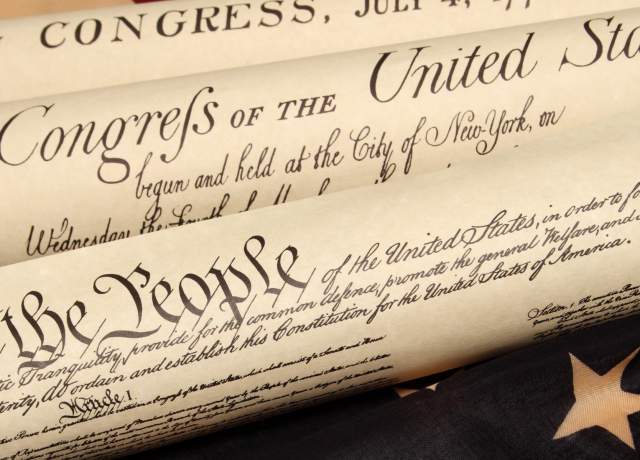 Close-up of rolled historic U.S. documents with visible text “We the People” and American flag