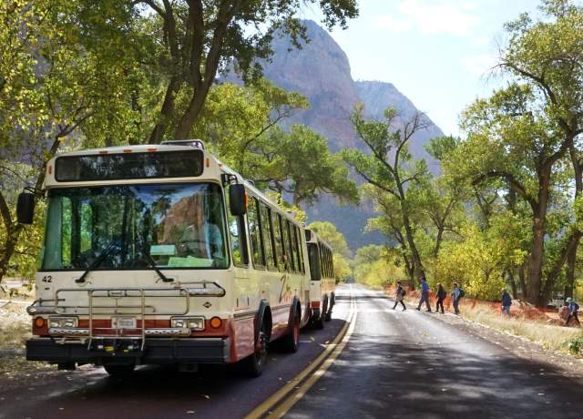 Scenic shuttle bus traveling through tree-lined canyon road with hikers and mountains near Cedar City and Brian Head