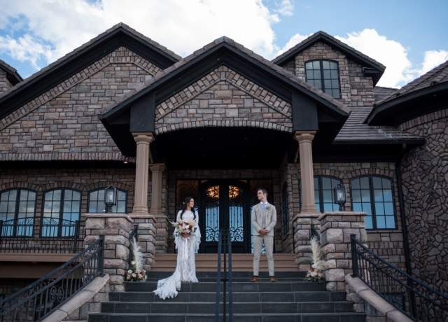 Couple stands on the front porch of the Cedar Rose Estate wedding venue in Parowan, Utah.