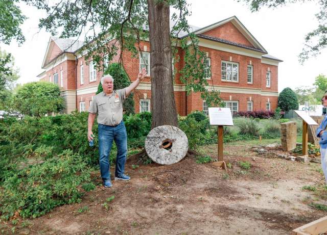 Older man standing in front of a building, talking to a small crowd of people