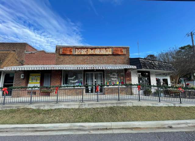 Old brick building with a sign that says Doris McDaniel, decorated for Christmas with window paintings and garland with red bows on the railing