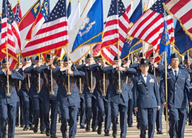 Group of military personnel marching while holding up assorted flags.