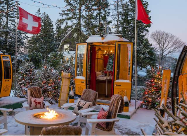 A swiss chalet in the snow with flags and fire pit.
