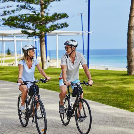 Couple cycling past Scarborough Beach, Sunset Coast