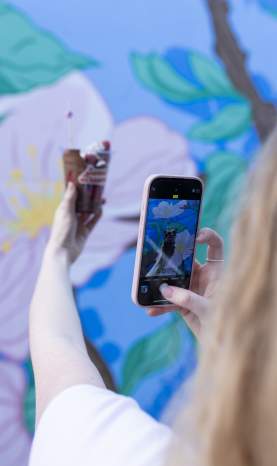 Capturing_Chocolate_Covered_Strawberry_Dessert_Photo_in_Front_of_a_Colourful_Floral_Mural_with_Phone
