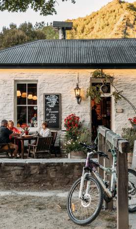 Old white cottage-looking pub with people sitting al fresco and green mountains in the background