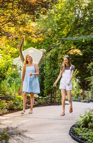 Two women walk along the paved path under a canopy of greenery at the Overland Park Arboretum & Botanical Gardens