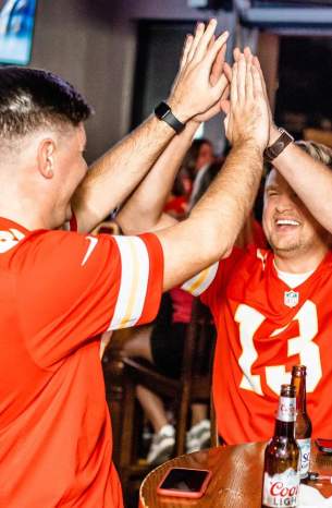Two men in Chiefs jerseys high five while watching the football game at Maloney's Bar & Grill