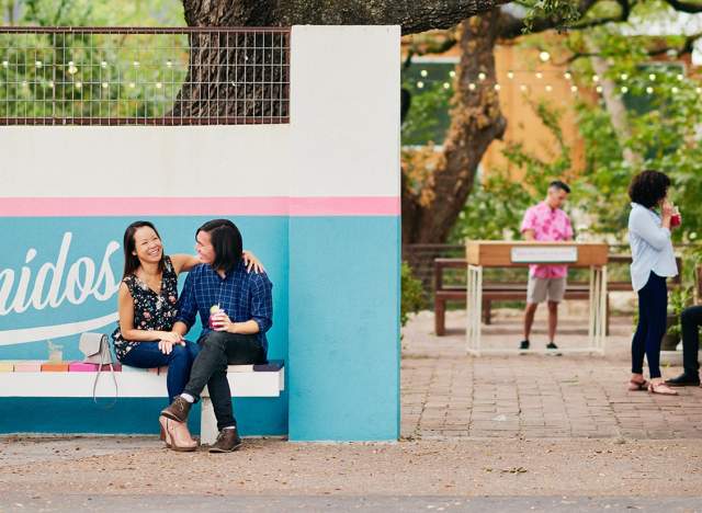 Couple sitting in front of Bienvenidos sign under live oak tree at Fresas outdoor patio in Austin Texas