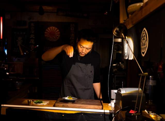 Chef Tatsu Aikawa sprinkles ingredients over a dish