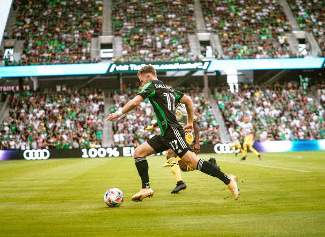 John Gallagher running with the ball at Q2 Stadium in front of a crowd.