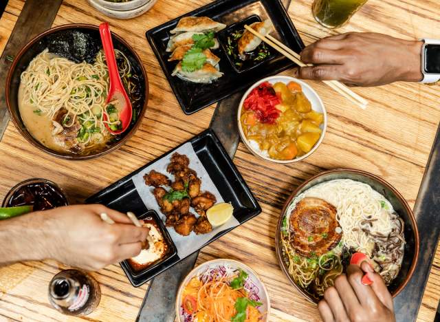 Hands reaching for different Ramen Tatsu-ya food items like ramen and crispy brussels sprouts.