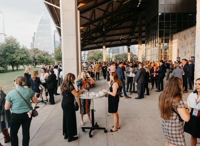 People with event badges on standing under the pavilion at Palmer Events Center during golden hour.