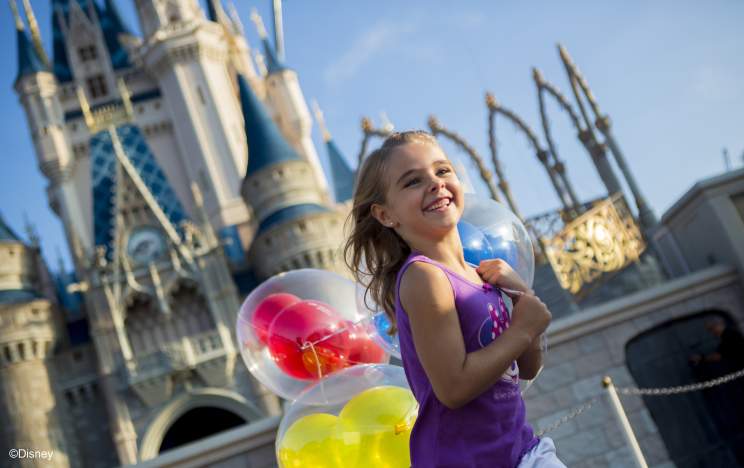Little girl holding balloons in front of Cinderella's Castle at Walt Disney World