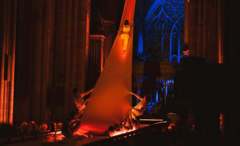 An event during Freedom Festival in Hull Minster with a dancer climbing up a long sheet held by 2 other performers