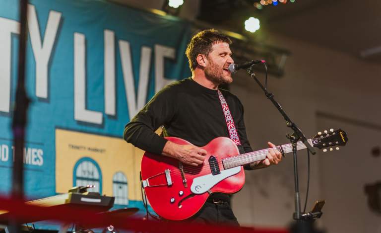 A man stands onstage with a bright red guitar. He sings into a microphone.