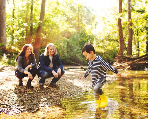 A lesbian couple watching their son play in a creek