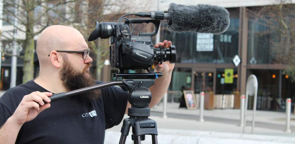 A person stood behind a camera filming in Guildhall Square